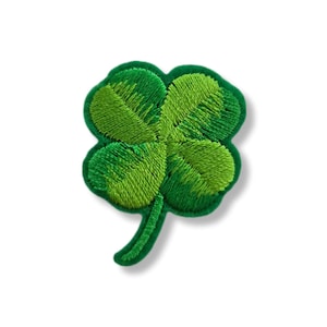 Puede incluir: Parche bordado de trébol de cuatro hojas en tonos verdes. El trébol tiene cuatro hojas en forma de corazón con costuras detalladas y un tallo verde. El parche es probablemente para ropa o accesorios.