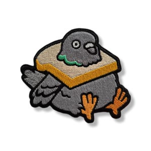 Peut inclure: Écusson brodé représentant un pigeon de dessin animé avec un sandwich autour du cou. Le pigeon est gris avec des pieds orange et un contour noir. Le sandwich a du pain beige et une croûte jaune.