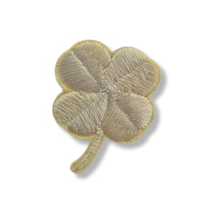 Puede incluir: Parche bordado de trébol de cuatro hojas en tonos beige y dorado. El trébol tiene cuatro hojas redondeadas con costuras detalladas y un pequeño tallo. Para ropa o accesorios.