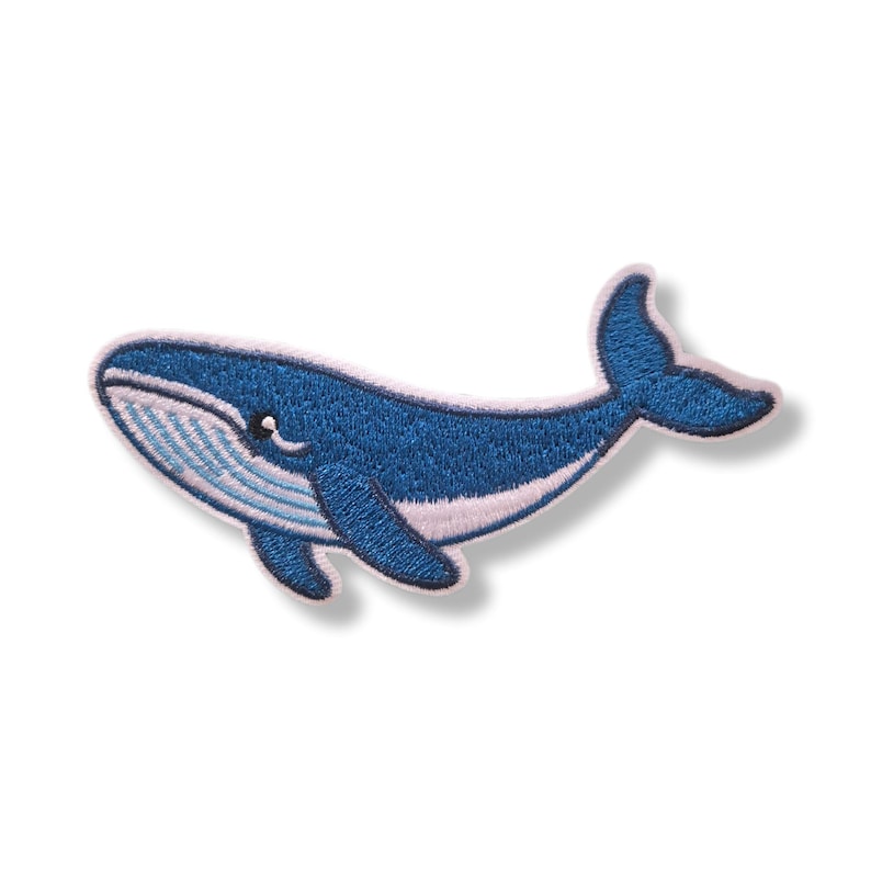 Op de afbeelding: Een geborduurde patch in de vorm van een blauwe vinvis met een donkerblauw lichaam en een lichtblauw en wit gestreepte buik. De walvis is afgebeeld in zwempositie met een zichtbaar oog, een borstvin en een staartvin, afgewerkt met een witte rand.