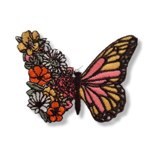 Può includere: Toppa a farfalla ricamata. Un'ala presenta una collezione di fiori arancioni, gialli e bianchi. L'altra ala ha sezioni rosa e gialle con contorni neri. La farfalla ha un corpo nero. Ideale per abbigliamento.