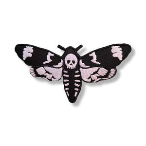 Peut inclure: Un écusson brodé noir et blanc en forme de papillon de nuit. Les ailes du papillon sont noires avec des détails blancs, et le corps présente un motif de crâne. Idéal pour les vêtements ou accessoires.