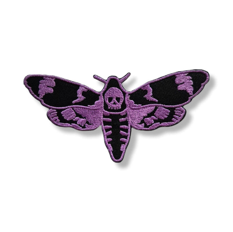 Peut inclure: &Eacute;cusson brod&eacute; repr&eacute;sentant un sphinx &agrave; t&ecirc;te de mort. Le papillon de nuit a des ailes noires avec des accents violets et un corps violet. La t&ecirc;te du papillon est un cr&acirc;ne. L'&eacute;cusson est probablement destin&eacute; aux v&ecirc;tements ou aux accessoires.