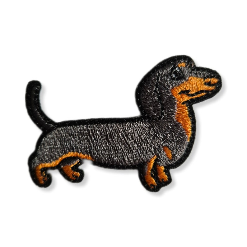 May include: Black and tan dachshund embroidered patch. The dachshund is facing right and has a long body and short legs.