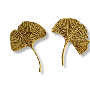 Può includere: Due foglie di ginkgo ricamate in oro, ciascuna con un delicato design a forma di ventaglio. Le foglie sono separate e hanno un aspetto leggermente testurizzato.
