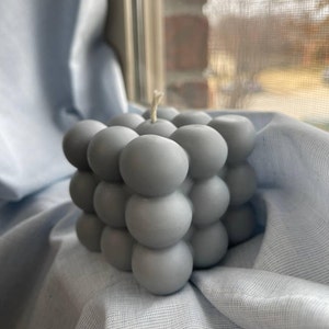 May include: A gray bubble candle with a round, textured surface. The candle is made of wax and has a single wick.