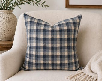Peut inclure: Un coussin carré décoratif avec un motif à carreaux bleu et beige. Le coussin est placé sur un fauteuil crème. Le coussin a un aspect doux et texturé, suggérant confort et style. C'est un article de décoration intérieure.