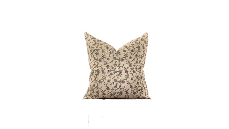 May include: A decorative throw pillow with a beige background and a repeating floral pattern in shades of brown, green, and burgundy. The pillow is square-shaped and has a soft, inviting appearance, suitable for home decor.