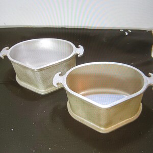 May include: Two silver aluminum baking dishes with handles. The dishes are shaped like a heart and have a textured surface.