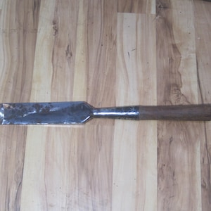 May include: A metal and wood chisel with a long, flat blade and a wooden handle. The blade is silver and the handle is brown.
