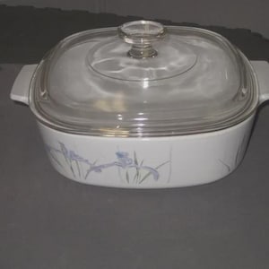 May include: White casserole dish with a clear glass lid. The dish has a floral design in shades of blue and purple. The lid has a clear glass knob. The dish has two white handles.