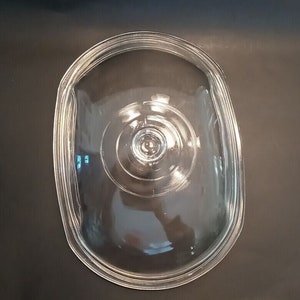 May include: Clear glass oval-shaped lid for a slow cooker. The lid has a knob on top.