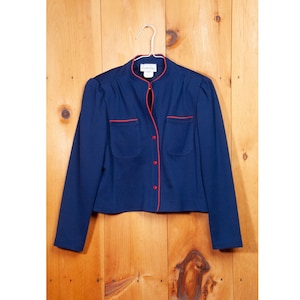 Puede incluir: Una chaqueta azul marino con ribetes rojos alrededor del cuello, los bolsillos y la tapeta de botones.