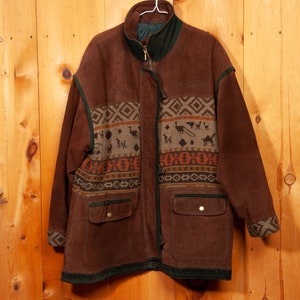 May include: A brown suede jacket with a geometric patterned fabric panel on the front. The jacket has a zipper closure and two pockets.