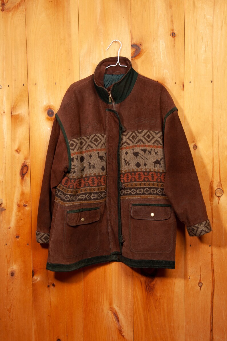 May include: A brown suede jacket with a geometric patterned fabric panel on the front. The jacket has a zipper closure and two pockets.