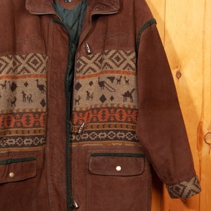 May include: A brown leather jacket with a geometric patterned design on the front and sleeves. The jacket has a zipper closure, two pockets, and a green lining. The label on the jacket reads "PELLE".