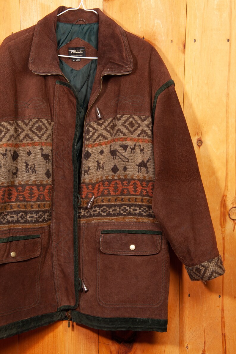 May include: A brown leather jacket with a geometric patterned design on the front and sleeves. The jacket has a zipper closure, two pockets, and a green lining. The label on the jacket reads "PELLE".