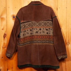 May include: A brown suede jacket with a green corduroy collar and cuffs. The jacket has a geometric pattern in shades of brown, orange, and beige on the back.