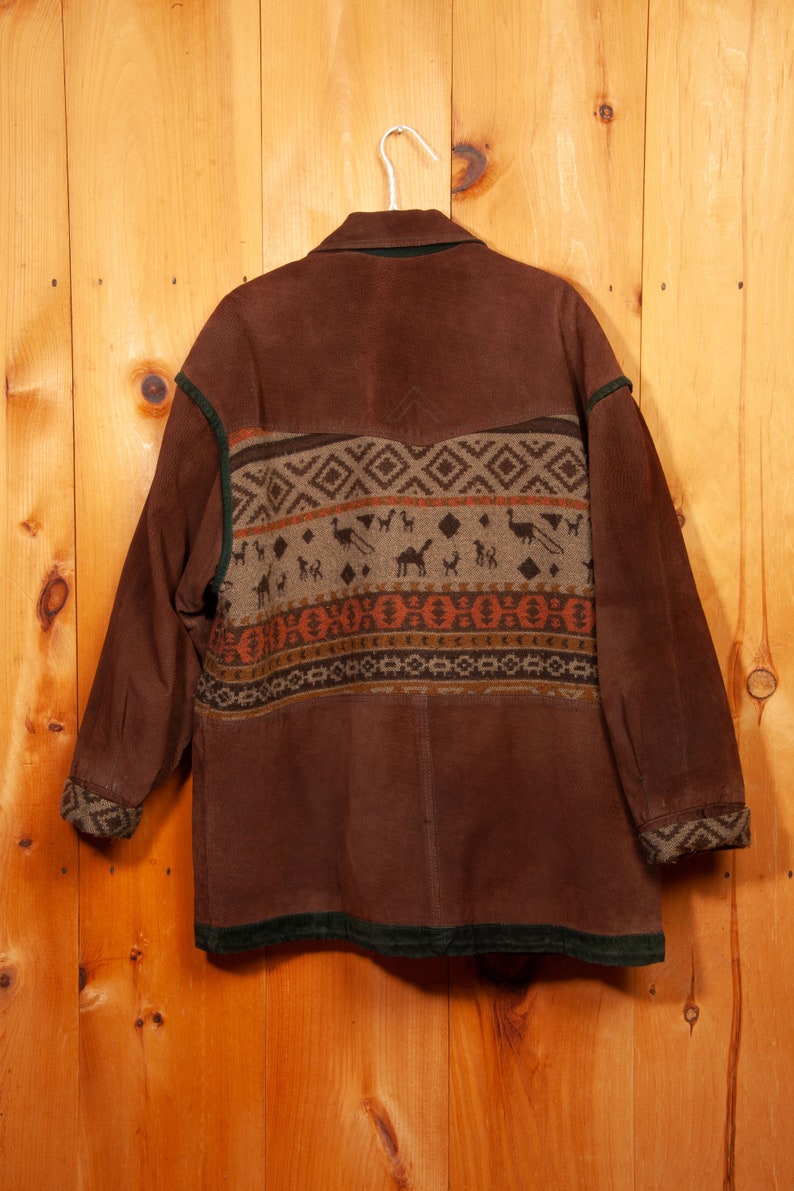 May include: A brown suede jacket with a green corduroy collar and cuffs. The jacket has a geometric pattern in shades of brown, orange, and beige on the back.