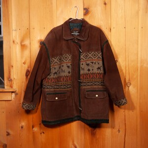 May include: A brown suede jacket with a green and brown patterned lining. The jacket has a zipper closure and two pockets.