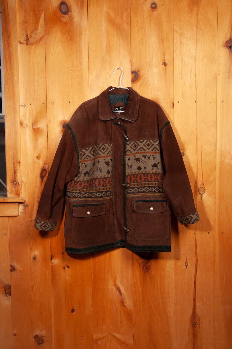 May include: A brown suede jacket with a green and brown patterned lining. The jacket has a zipper closure and two pockets.