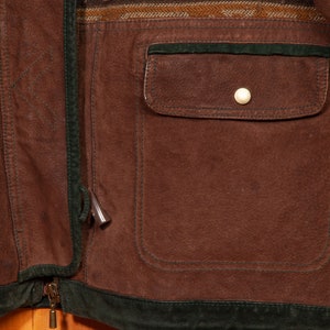 May include: A brown leather jacket with a green suede trim and a zipper closure. The jacket has a large pocket on the front and a patterned fabric panel on the top.