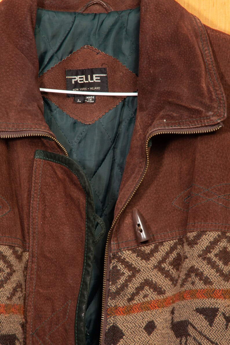 May include: A brown suede jacket with a zipper closure and a patterned fabric lining. The jacket has a label that reads "PELLE NEW YORK - MELAND" and "MADE IN CHINA".