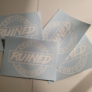 May include: Four blue stickers with white text that reads "Certified Ruined" in a circle. The stickers are on a white surface.
