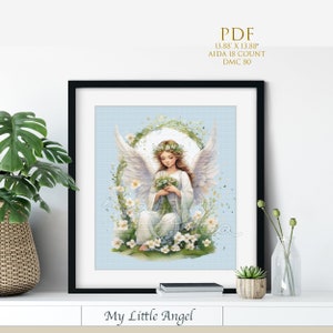 May include: A cross stitch pattern featuring a little angel with wings, a flower crown, and a bouquet of flowers. The angel is sitting in a wreath of flowers on a light blue background. The pattern is titled "My Little Angel".