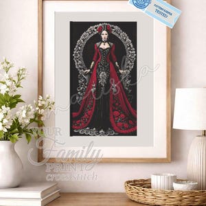 May include: Framed cross-stitch art featuring a woman in a red and black gown, surrounded by a floral wreath. The artwork is displayed in a wooden frame and rests on a wooden surface. The text "YOUR Family PRINT cross stitch" is visible.