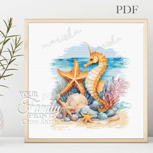 May include: Cross-stitch pattern featuring a seahorse, starfish, and seashells on a sandy beach with blue water and coral. The artwork is framed in a gold-colored frame. The text "mariska" and "Your Family Print Cross Stitch" are visible.