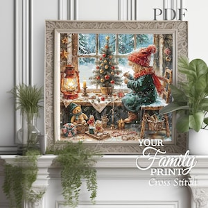 Puede incluir: Una obra de arte de punto de cruz enmarcada representa una escena invernal acogedora. Un niño con gorro rojo y abrigo verde decora un árbol de Navidad junto a una ventana nevada. Una linterna, osos de peluche y adornos se suman al ambiente festivo. El texto "YOUR Family PRINT Cross Stitch" es visible.