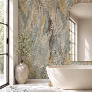 May include: Wallpaper featuring a large-scale botanical pattern of overlapping tropical leaves in muted shades of sage green, soft blue, and warm gold. The design covers the wall behind a white freestanding bathtub and a tall gold faucet.