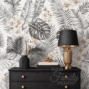 May include: A black dresser with a black lamp, a white orchid in a black vase, and a gold decorative object. The wall features wallpaper with a black and white botanical print of palm leaves and orchids, with the text Your Family Print.
