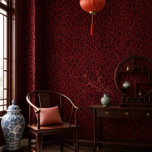 May include: A room interior featuring deep red leopard print wallpaper, a dark wood chair with a solid red cushion, a matching dark wood console table with a circular display shelf, a blue and white porcelain jar, and a red hanging lantern.