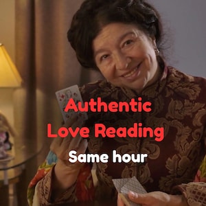 Könnte beinhalten: Eine Frau hält Spielkarten, mit dem Text "Authentic Love Reading Same hour" in Rot. Sie trägt ein gemustertes bordeauxfarbenes Oberteil. Eine Lampe und ein kleines dekoratives Objekt sind im Hintergrund zu sehen. Das Bild deutet auf eine Wahrsageberatung hin.