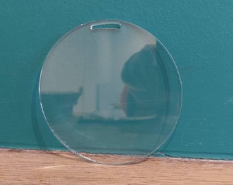 May include: A clear round acrylic blank ornament with a hole at the top for hanging.