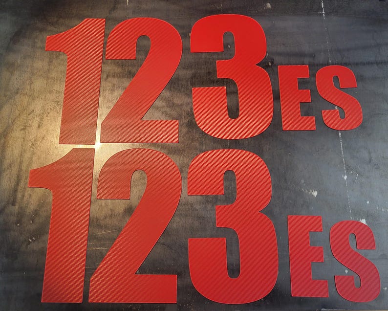 以下が含まれることがあります： 赤い数字123と「ES」という単語が、太字の赤いカーボンファイバーのようなフォントで書かれています。