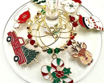 May include: Set of eight gold-tone Christmas-themed wine glass charms. The charms feature a snowman, a reindeer, a candy cane, a Christmas tree, a Santa hat, a mitten, a truck, and a Santa hat.