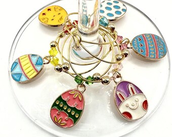 May include: Set of six gold-tone Easter egg-shaped wine glass charms. Each charm features a different colourful Easter egg design, including a bunny rabbit.