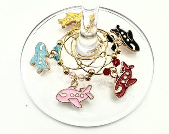 May include: Set of six colorful airplane-shaped wine glass charms. Each charm features a different color airplane with a gold ring.