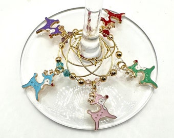 May include: Set of six gold-tone reindeer wine glass charms with colorful enamel accents. Each charm features a different color reindeer with a red nose and white spots. The charms are attached to gold-tone rings with clear beads.