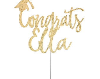 May include: Gold glitter graduation cake topper with the text "Congrats Ella" and a graduation cap.