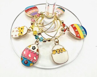 May include: Set of six gold-tone Easter egg-shaped wine glass charms with colourful enamel designs. The charms are attached to a gold-tone chain with colourful beads.