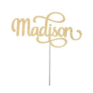 May include: Gold glitter cake topper with the name "Madison" in a cursive font.
