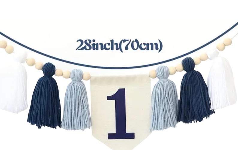 K&ouml;nnte beinhalten: Ein wei&szlig;es Banner mit der Zahl 1 in Blau, umgeben von einer Girlande aus Holzperlen und blauen und wei&szlig;en Garnquasten. Das Banner ist 70 cm lang.