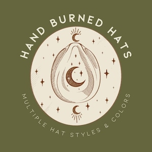 May include: Olive green background with a circular logo featuring the text "HAND BURNED HATS" and "MULTIPLE HAT STYLES & COLORS". The logo includes a central design of an avocado shape with crescent moons and stars.