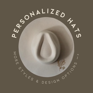 Puede incluir: Un sombrero fedora color crema con una corona en forma de lágrima y un ala ancha. El texto "PERSONALIZED HATS" está arqueado sobre el sombrero, con "MORE STYLES & DESIGN OPTIONS" debajo. Un pequeño logotipo está en el sombrero.