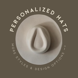 Puede incluir: Un sombrero fedora de color claro con una corona en forma de lágrima, centrado sobre un fondo marrón. El texto "PERSONALIZED HATS" está dispuesto en círculo alrededor del sombrero. El texto adicional dice "MORE STYLES & DESIGN OPTIONS".