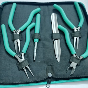 May include: A set of jewelry-making tools, including pliers with teal handles, a mandrel, and a knife-like tool, neatly arranged in a black zippered case with teal trim. The tools are secured with black elastic straps.